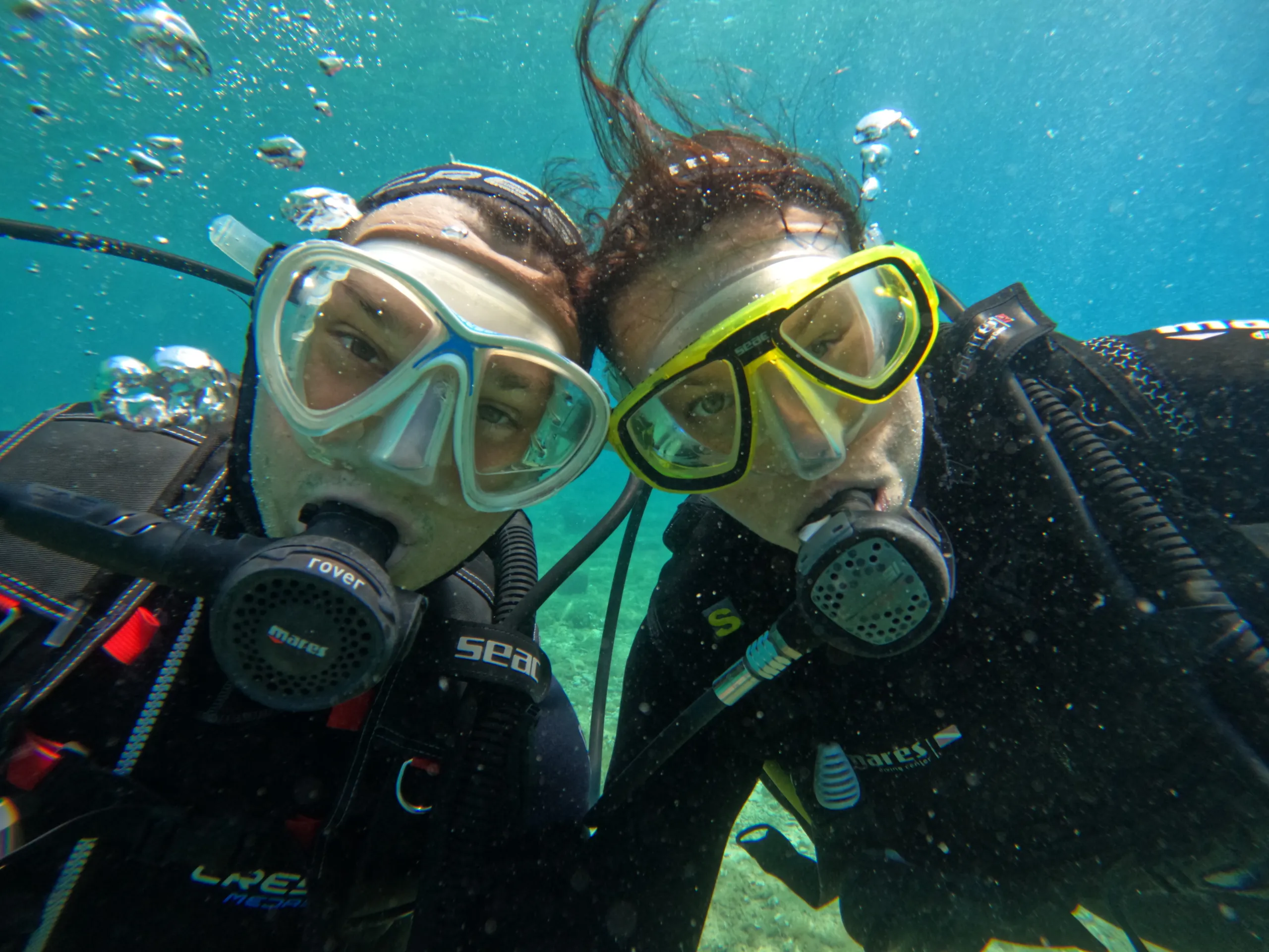 Two scuba divers in masks and regulators posing together underwater