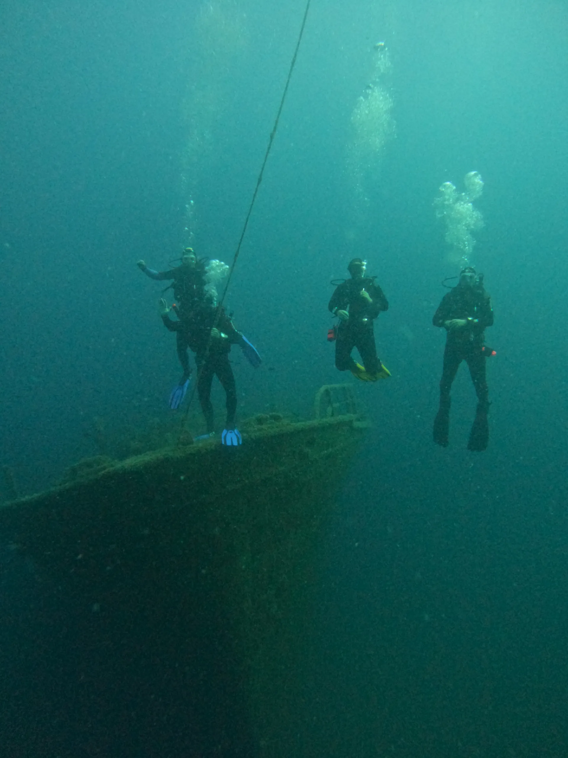 A group of scuba divers hovering above a submerged structure in blue-green water
