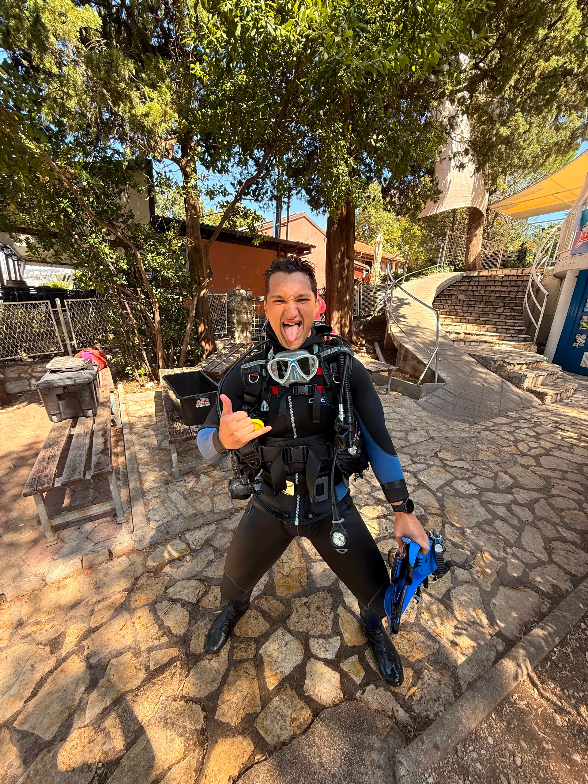 A diver in scuba equipment making a playful hand gesture outdoors