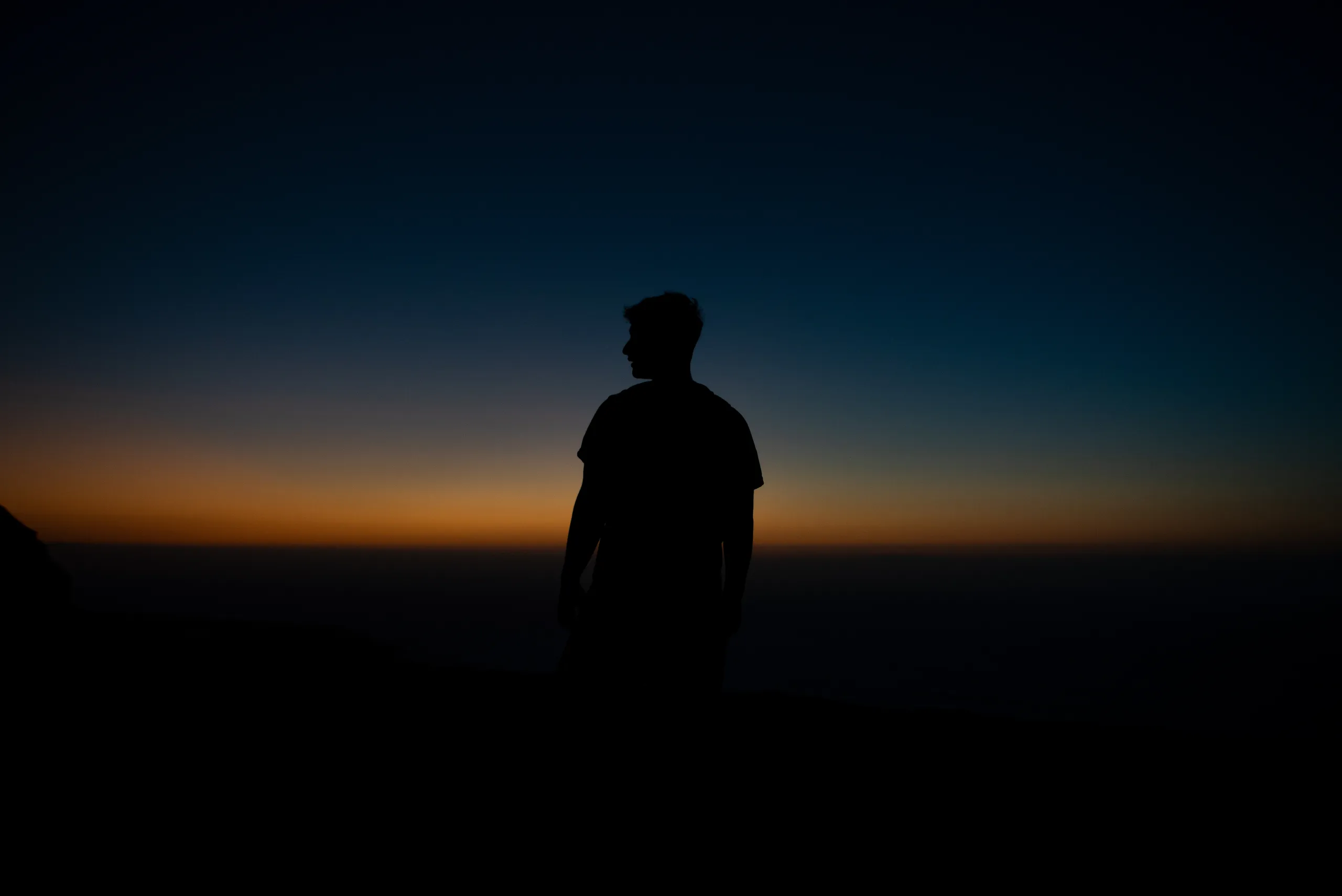 A person silhouetted against a deep blue sky and an orange sunset horizon