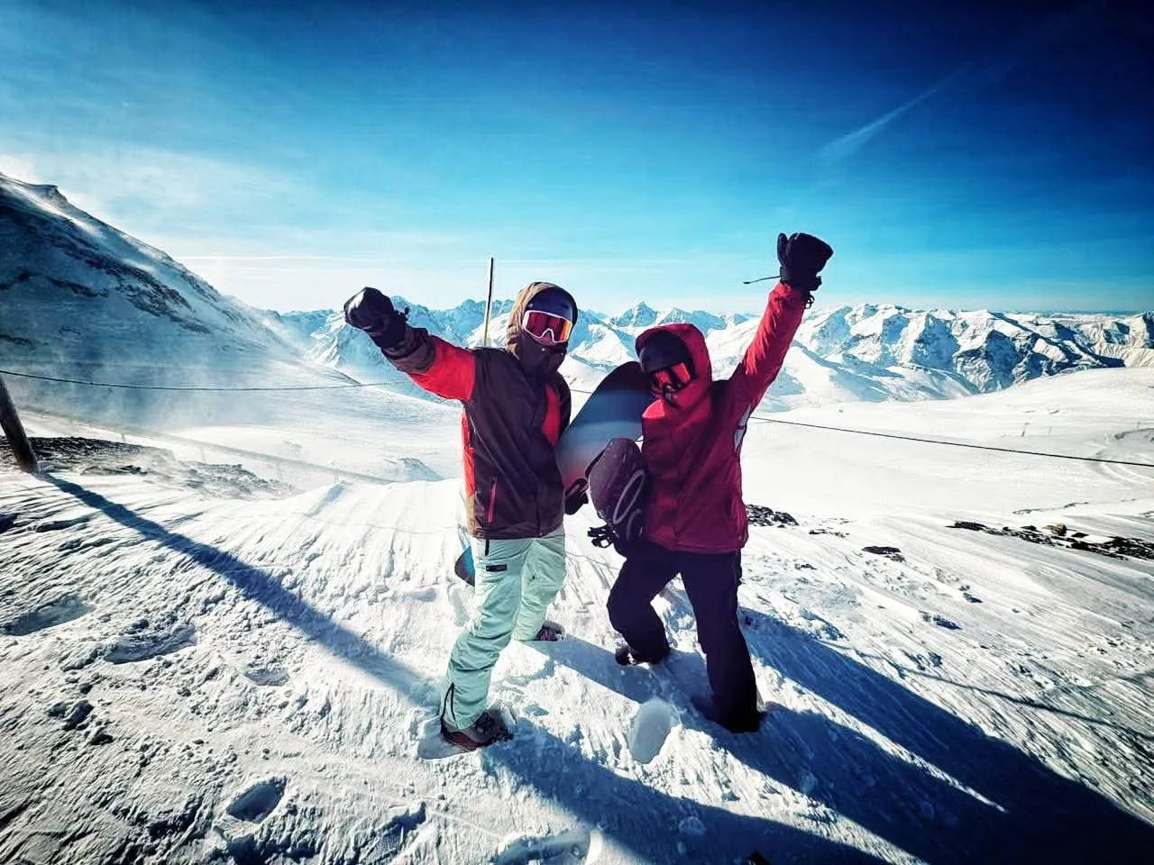 Two snowboarders raising their arms on a snowy mountain slope