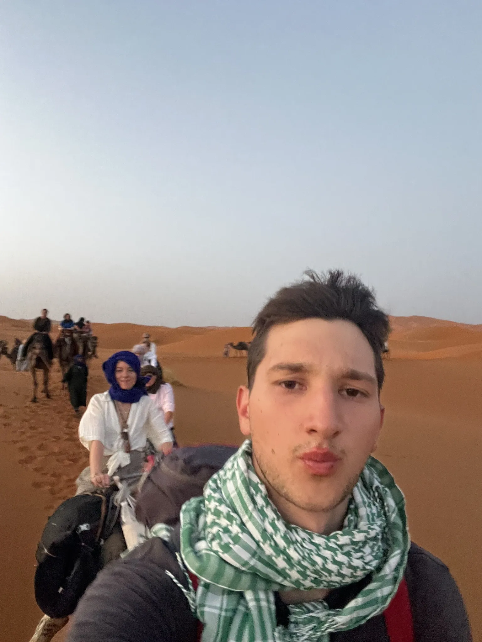A traveller in a patterned scarf taking a selfie with a group in the desert