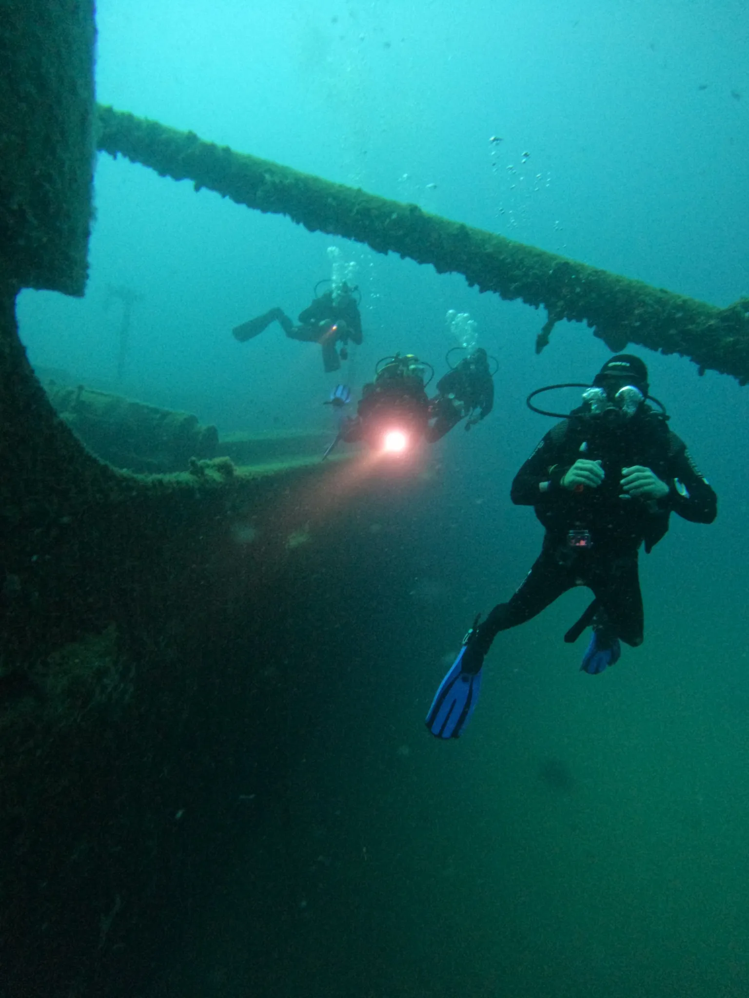 Scuba divers exploring a submerged structure in blue-green water