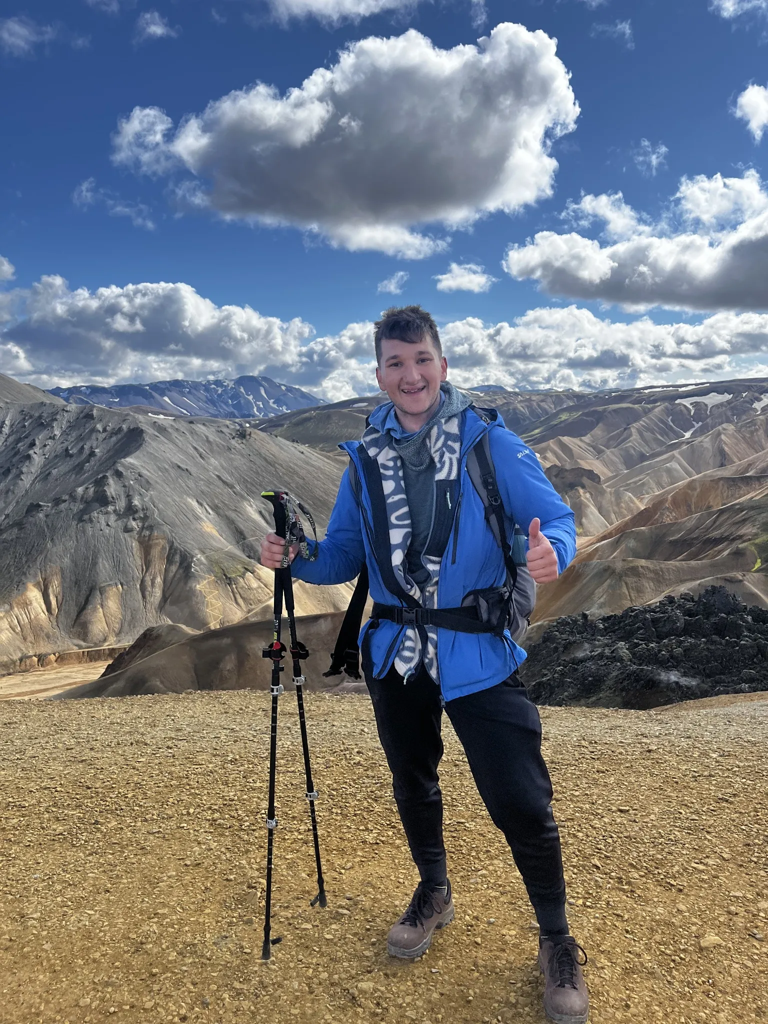 A hiker with trekking poles before rugged mountains and clouds