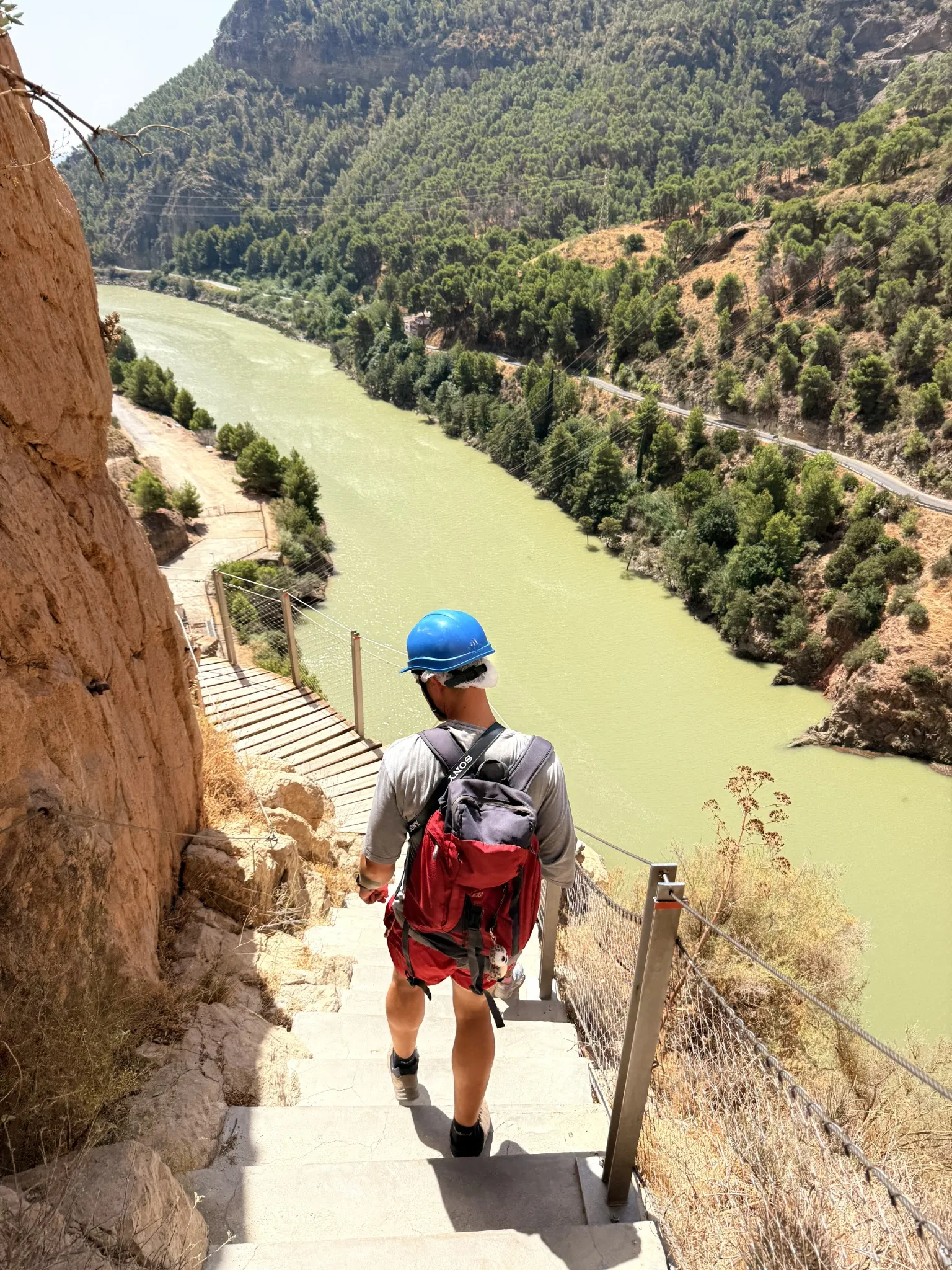 A helmeted hiker on a narrow cliffside walkway above a river