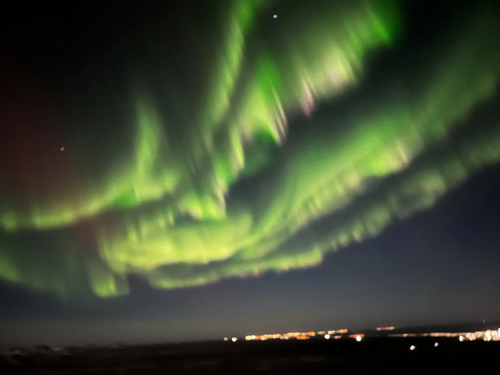 Bright green northern lights sweeping across a dark night sky