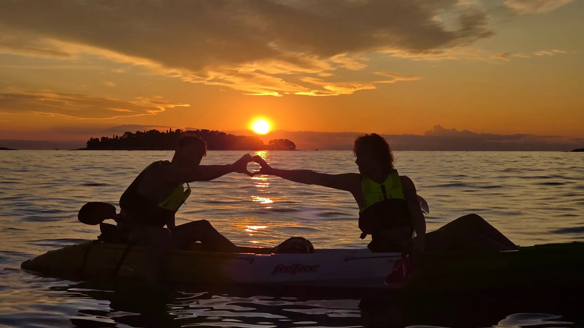 Two people in kayaks silhouetted against an orange sunset over the sea