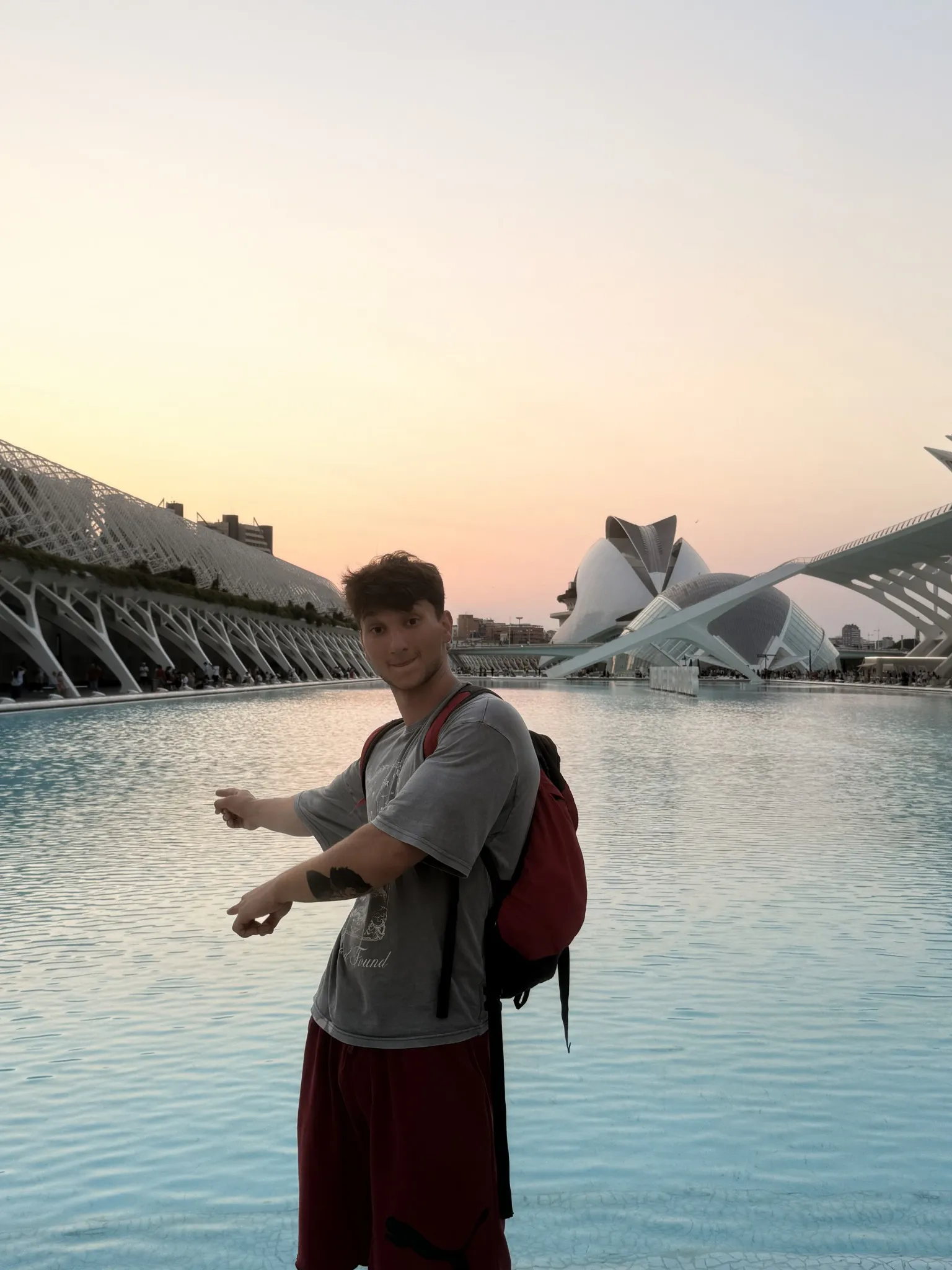 A traveller beside a reflecting pool and curved modern architecture at sunset