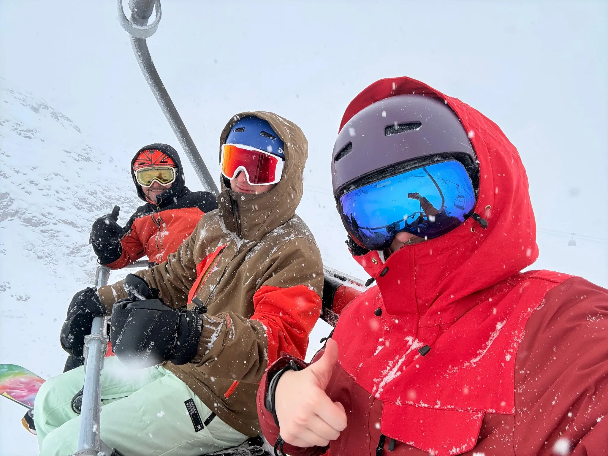 Three snowboarders wearing helmets and goggles on a ski lift