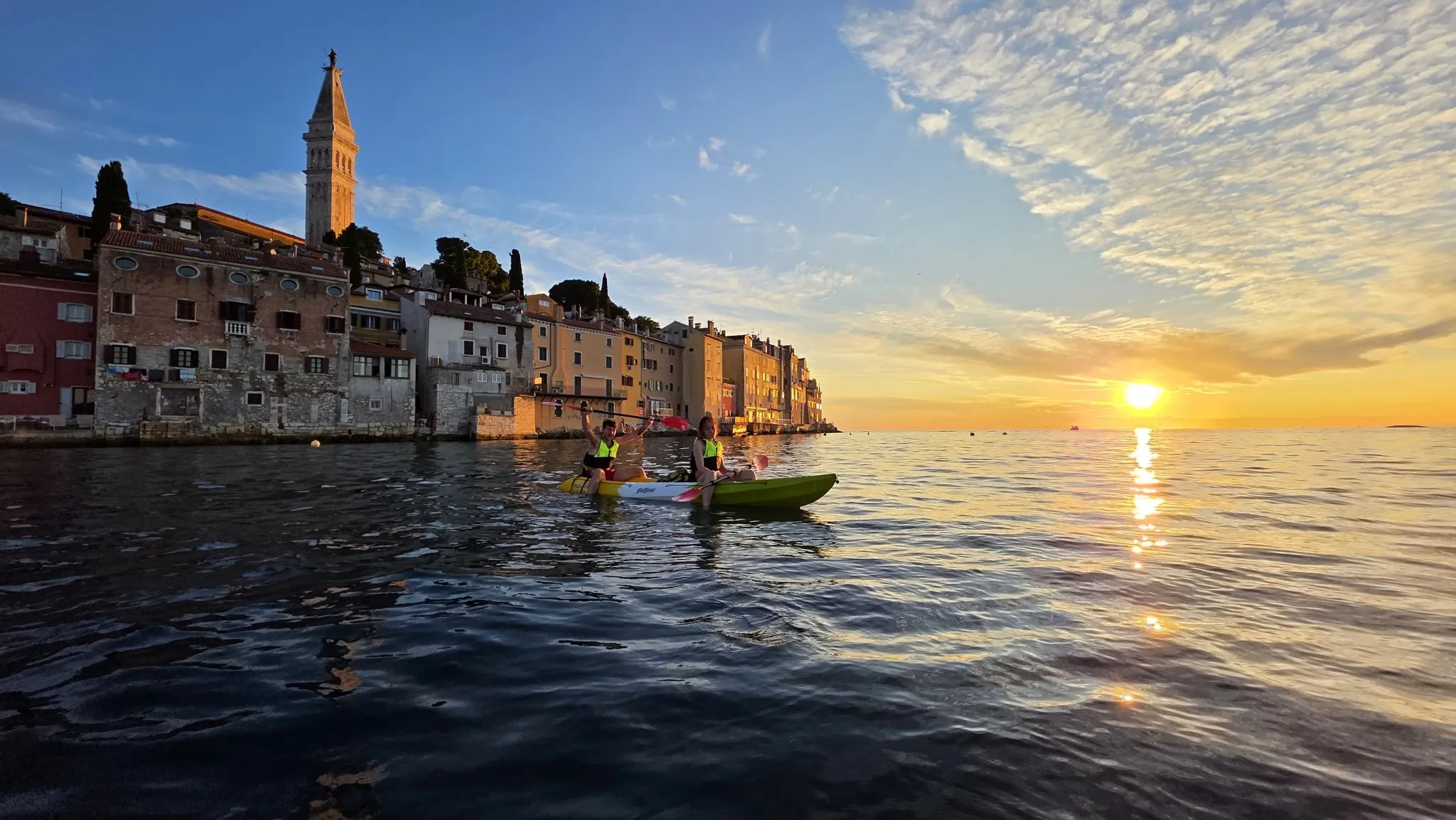 Kayakers on calm water beside a coastal town at sunset