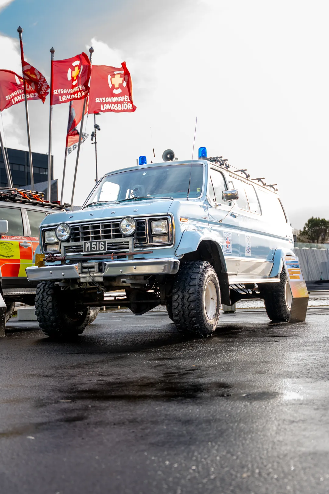 A blue Icelandic rescue vehicle with large tires beneath red rescue flags